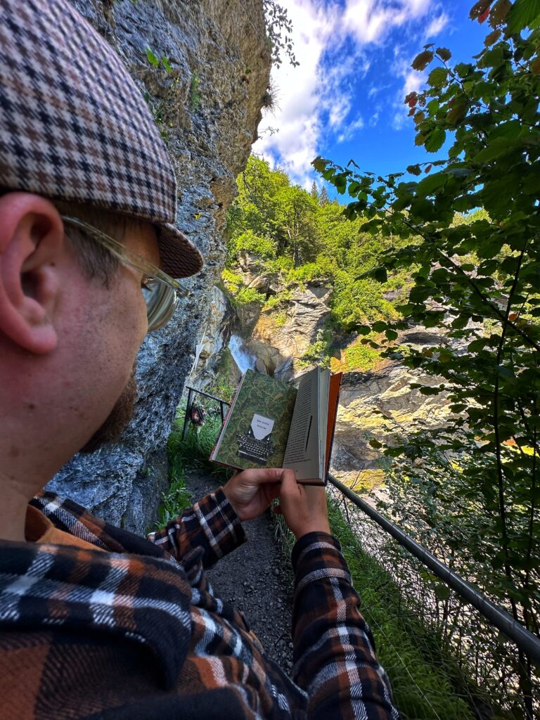 Phil liest ein Sherlock Holmes Buch mit Blick auf die Reichenbachfälle und die Felsschlucht
