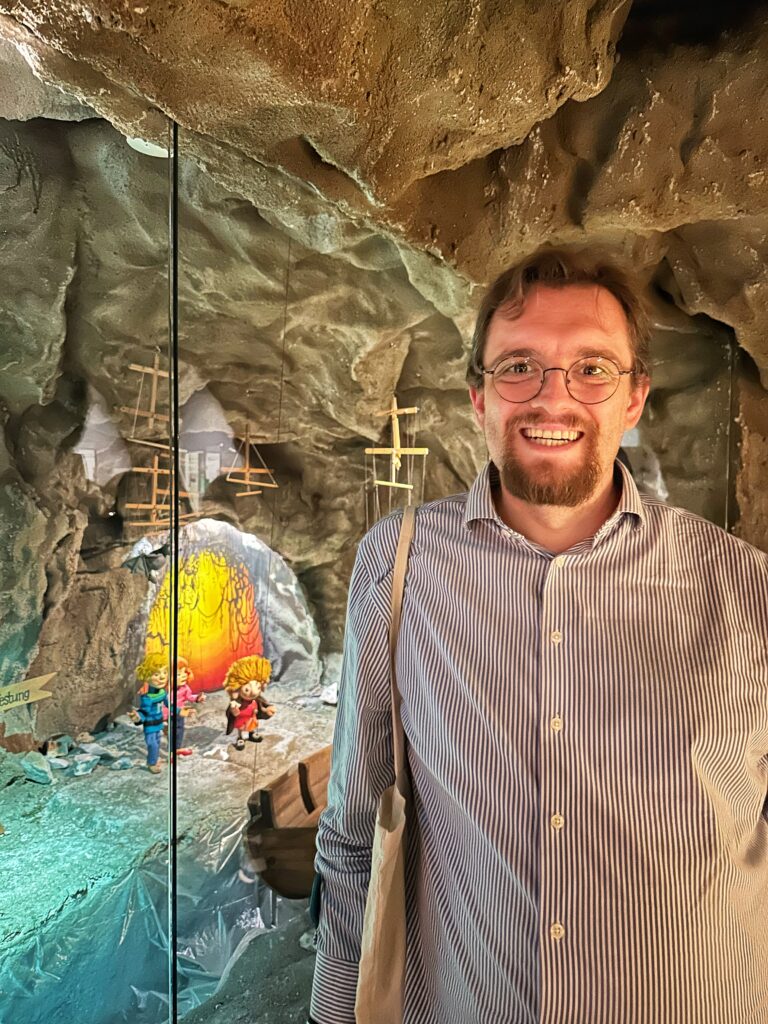 Phil von reisenstattrasen.de lächelt im Augsburger Puppenkiste Museum vor einer Felsenkulisse und Puppen.