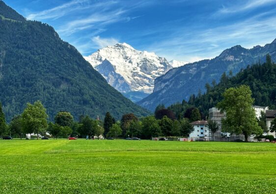 Große grüne Wiese der Höhenmatte in Interlaken mit schneebedeckten Bergen und blauem Himmel mit Wolken