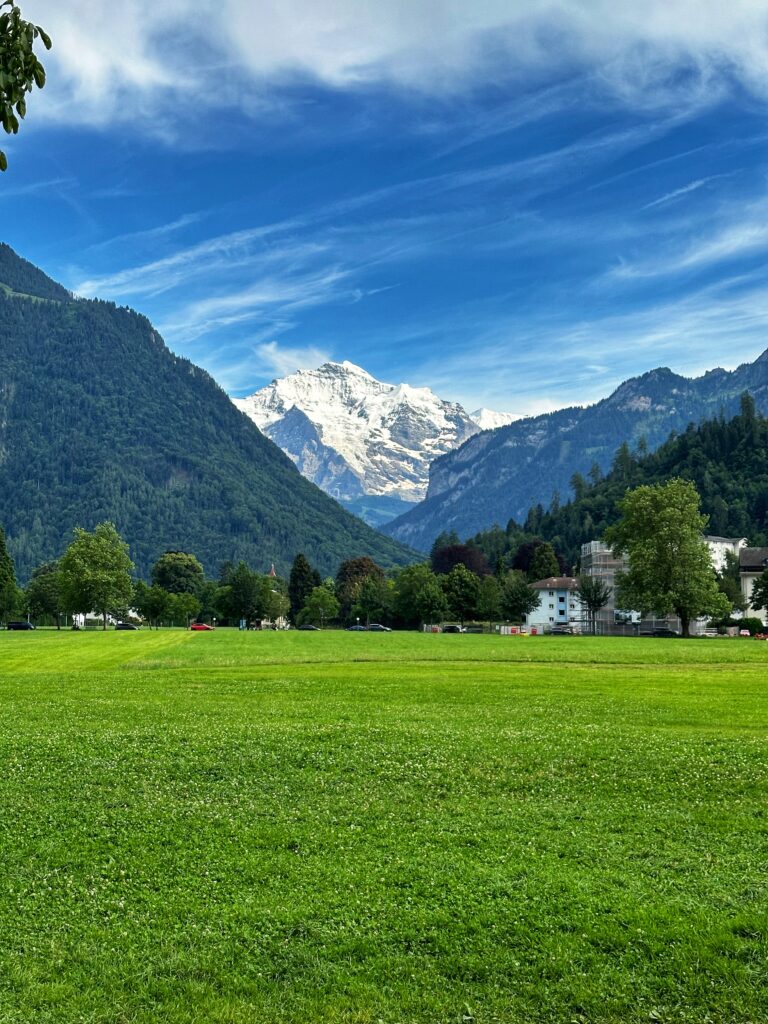 Große grüne Wiese der Höhenmatte in Interlaken mit schneebedeckten Bergen und blauem Himmel mit Wolken