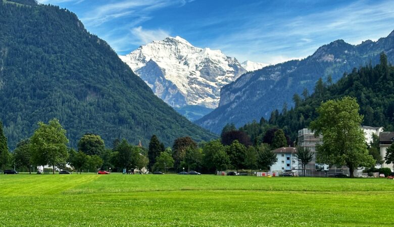 Große grüne Wiese der Höhenmatte in Interlaken mit schneebedeckten Bergen und blauem Himmel mit Wolken