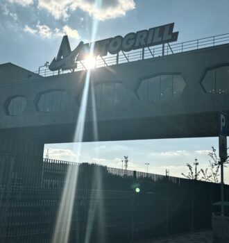 Aussicht auf das architektonische Brückenrestaurant Autogrill Limenella über der Autobahn, mit strahlendem Sonnenlicht und dem "AUTOGRILL"-Schriftzug.