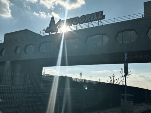 Aussicht auf das architektonische Brückenrestaurant Autogrill Limenella über der Autobahn, mit strahlendem Sonnenlicht und dem "AUTOGRILL"-Schriftzug.