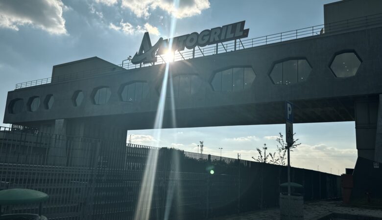 Aussicht auf das architektonische Brückenrestaurant Autogrill Limenella über der Autobahn, mit strahlendem Sonnenlicht und dem "AUTOGRILL"-Schriftzug.